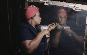 WWII color image of black woman setting rivets in aircraft section