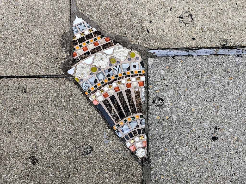 Street artist Ememem has carefully filled a break in the sidewalk with colorful bits of tile.