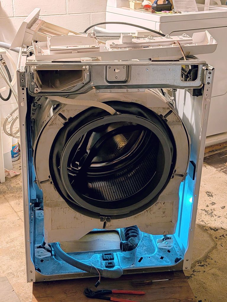 Kenmore front-loader washer with panels removed.  Interior is illuminated and pump has been removed. 